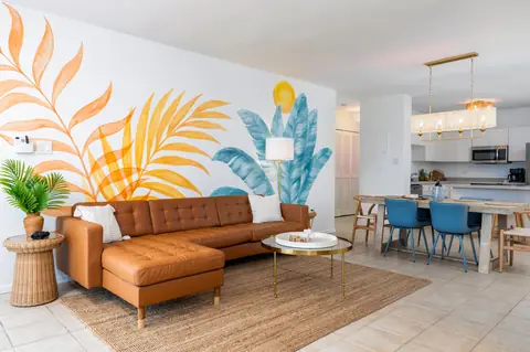 Living room with tropical leaf mural and leather sectional — Penthouse Vista Del Mar oceanfront rental in Isabela, Puerto Rico